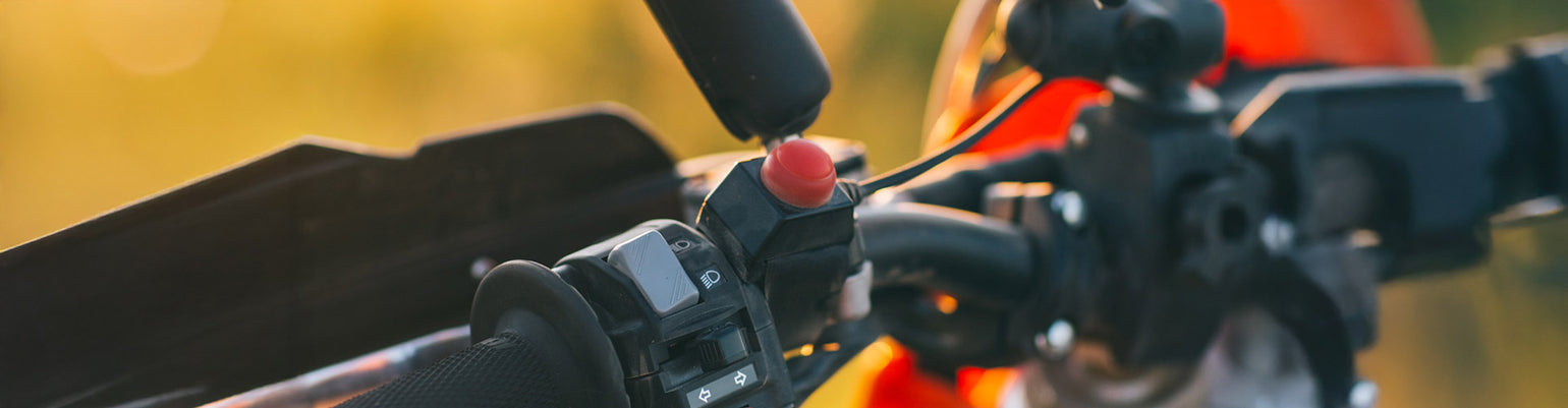 Rugged Radios Collection motorcycle handlebar PTT—red push‑to‑talk button perch‑mounted on handlebars with quick‑connect cord for Moto communication
